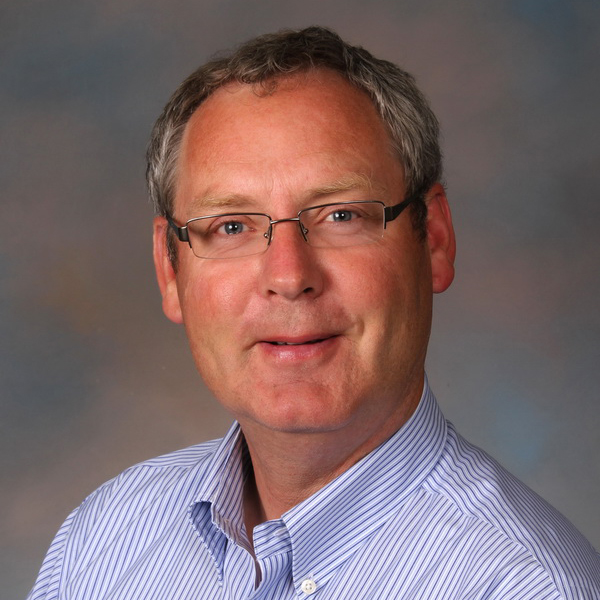 Portrait of Michael Scrimsher against a mottled blue and pink background.